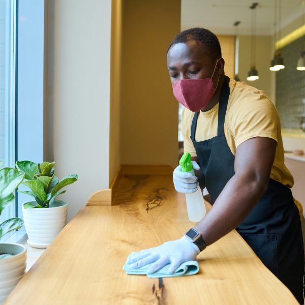 African waiter cleaning the table with spray disinfectant on table in restaurant during pandemic