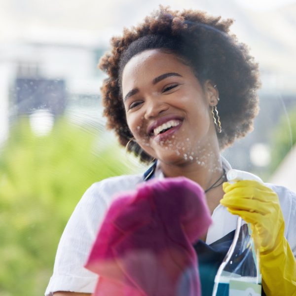 Black woman, cleaning spray and bottle on windows with cloth for hygiene of bacteria, dust and germs. Happy cleaner, housekeeping and chemical liquid for dirt, glass surface and hospitality services.